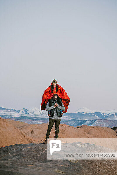 A woman sits on her friend's shoulders while laughing in the mountains