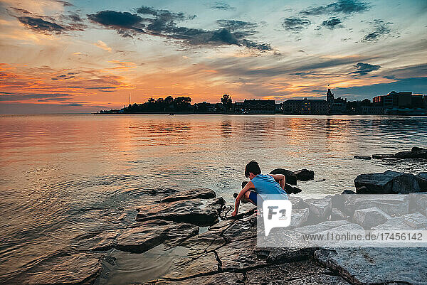 Young child playing on a rocky shoreline of Lake Ontario at sunset.