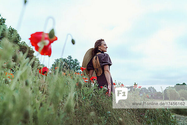 Woman with hat standing among poppies field against sky
