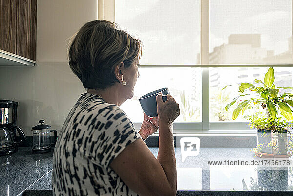 Mature Latin woman looking at the window drinking coffee