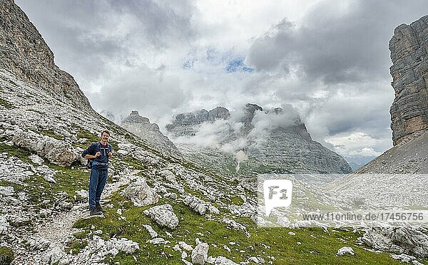Hiker  climber on a hiking trail between cloudy rocky mountains at Forcella Grande  Sorapiss circumnavigation  behind mountain Punte Tre Sorelle  Dolomites  Belluno  Italy  Europe