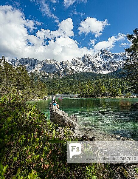 Young man sitting on a rock  view into the distance  Eibsee lake and Zugspitze in spring with snow  Wetterstein Mountains  near Grainau  Upper Bavaria  Bavaria  Germany  Europe