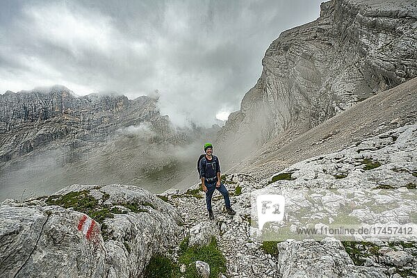 Hiker  climber on a trail between rocky cloudy mountains at Forcella Sore de la Cengia  Sorapiss circumnavigation  Dolomites  Belluno  Italy  Europe