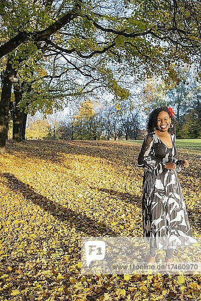 Portrait of a smiling  dark-skinned woman with curls in a dress  outdoor shot in autumn  Germany  Europe