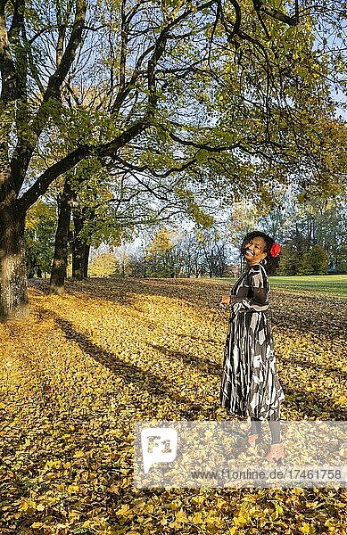 Portrait of a smiling  dark-skinned woman with curls in a dress  outdoor shot in autumn  Germany  Europe