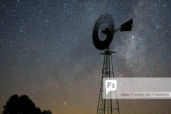 View of aermotor windmill spinning against milky way in sky