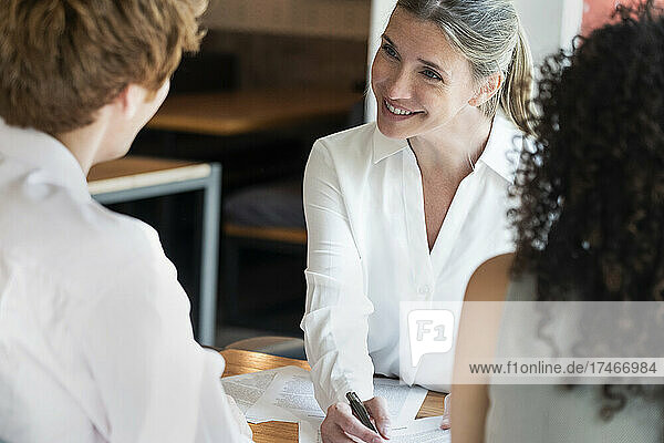 Smiling mature woman talking to young couple in office