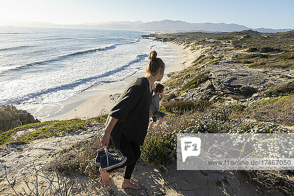 A teenage girl and her brother running down a path towards a sandy beach