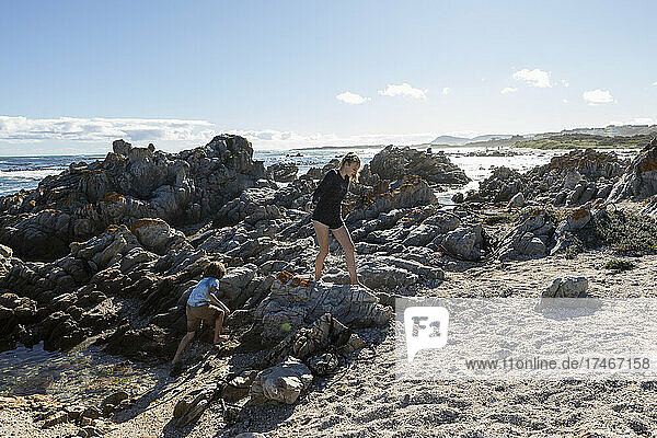 Two children  a teenage girl and eight year old boy exploring the jagged rocks and rockpools on a beach.