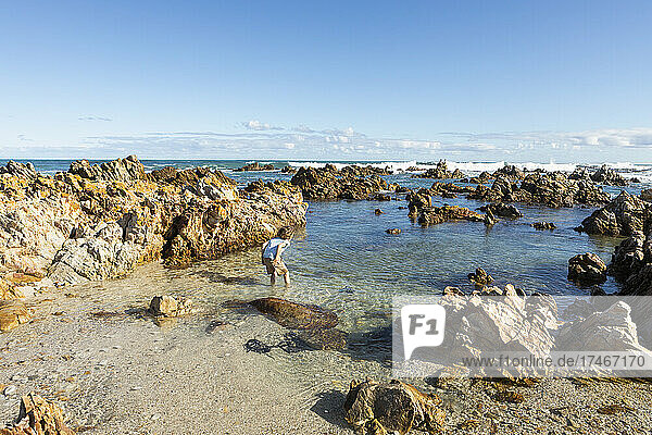 Young boy exploring a beach and rockpools on a jagged rocky coastline.