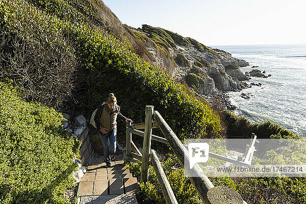 Erwachsene Frau  die eine Treppe zur Klippe oberhalb eines Strandes hinaufgeht.