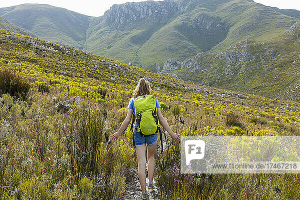 Ein Mädchen im Teenageralter  das mit einem Rucksack einen Pfad in den Bergen entlangläuft
