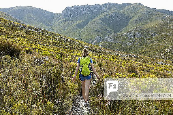 Ein Mädchen im Teenageralter  das mit einem Rucksack einen Pfad in den Bergen entlangläuft