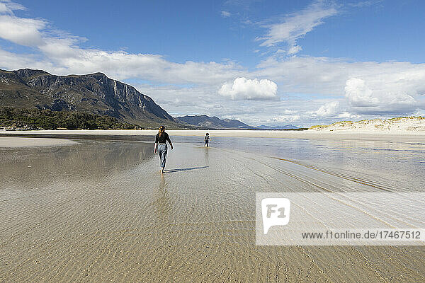 Teenage girl and younger brother walking through shallow water on a sandy beach