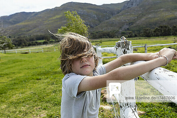 Achtjähriger Junge lehnt an einem Zaun und sieht sich Pferde auf einem Feld an