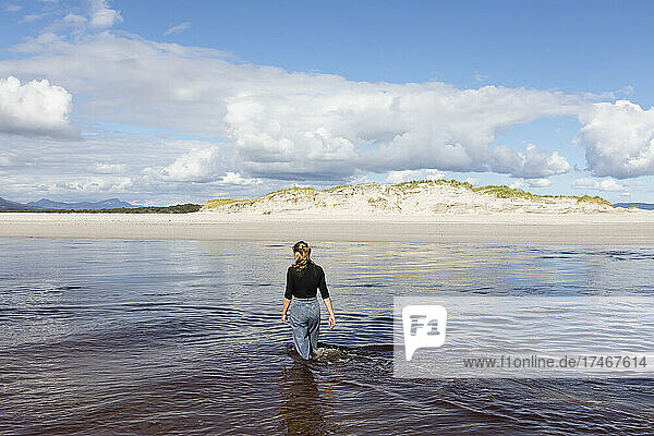 Ein junges Mädchen watet durch einen Wasserkanal an einem breiten Sandstrand.