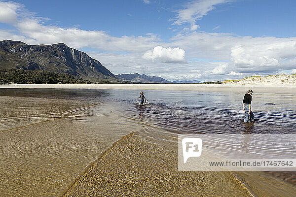 Teenager-Mädchen und Junge an einem offenen Sandstrand  die durch flaches Wasser waten.