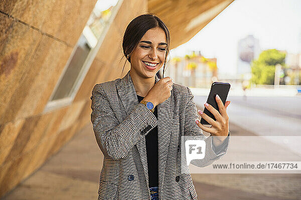 Happy businesswoman talking during video conference through mobile phone on footpath