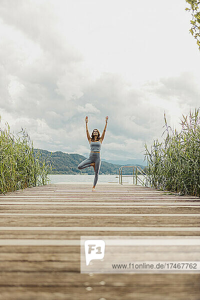 Woman with arms raised doing yoga on jetty