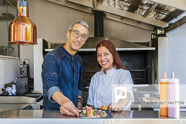 Smiling male and female chefs with tray at restaurant