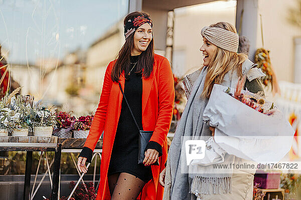 Smiling woman walking with friend by flower shop