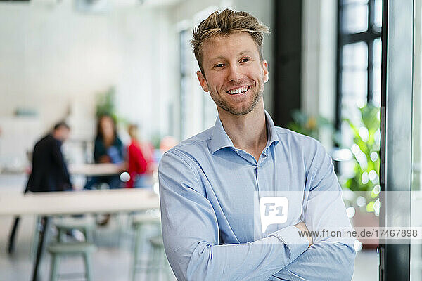 Young smiling businessman with arms crossed at office