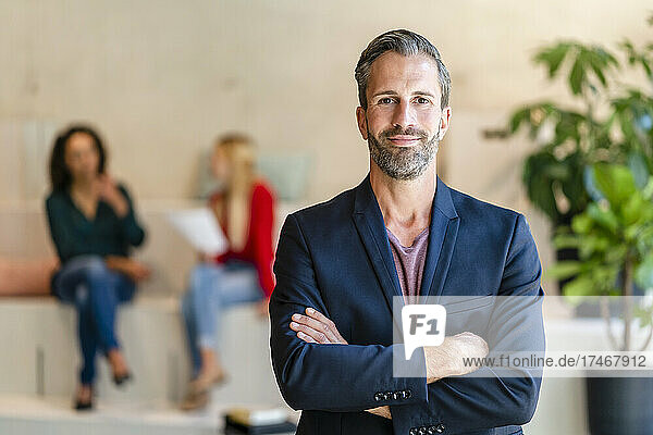 Smiling bearded businessman with arms crossed in office