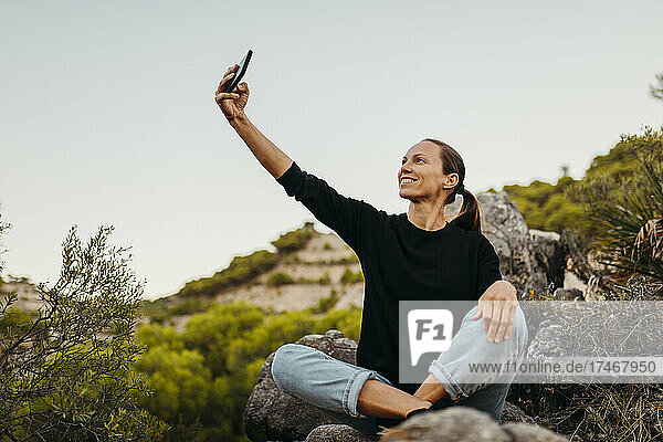 Smiling woman taking selfie through mobile phone on rock