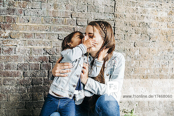Daughter kissing mother in front of brick wall