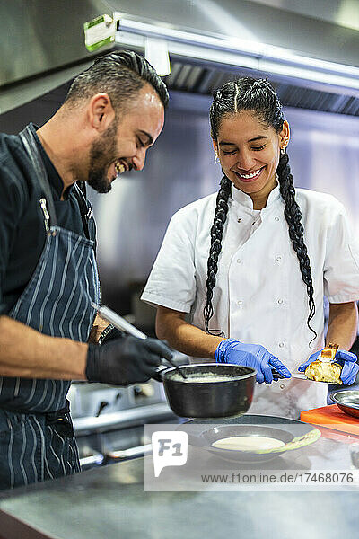 Smiling chef and trainee plating food in commercial kitchen