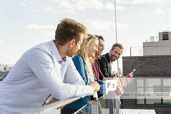 Happy coworkers holding drink bottles while leaning on railing