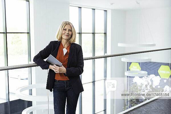 Mature female professional with digital tablet standing by railing