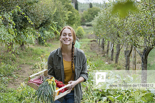 Happy female farmer holding fresh vegetables in garden