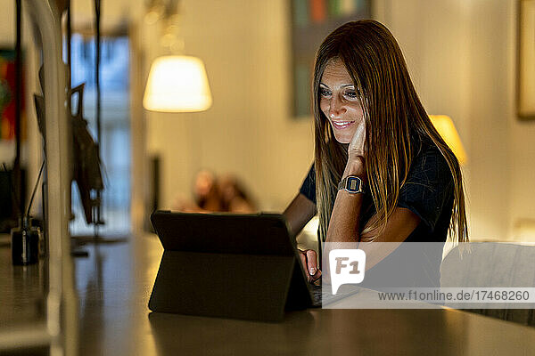 Lächelnde Frau mit der Hand am Kinn  die zu Hause einen Laptop benutzt