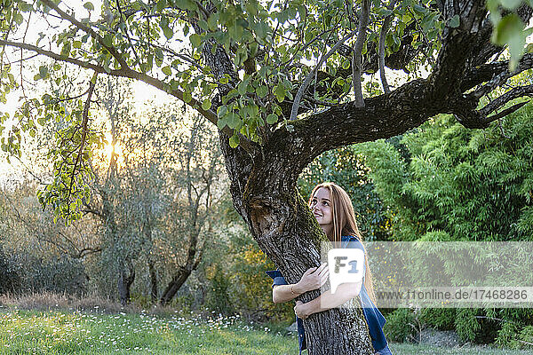 Lächelnde Frau umarmt einen Baum auf dem Land