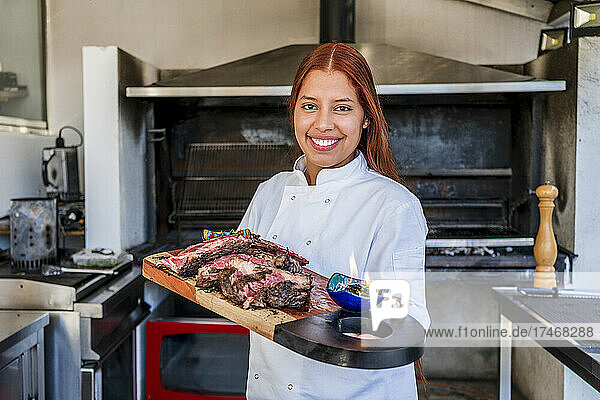 Smiling female chef holding cutting board in kitchen
