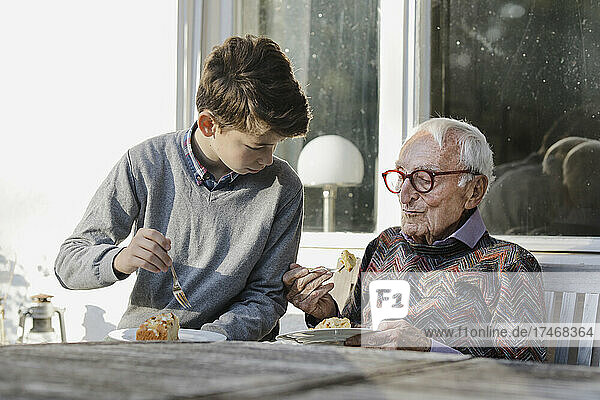 Boy with grandfather having food at table