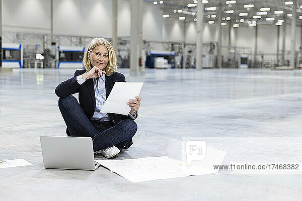 Mature female professional with document sitting on ground in industry
