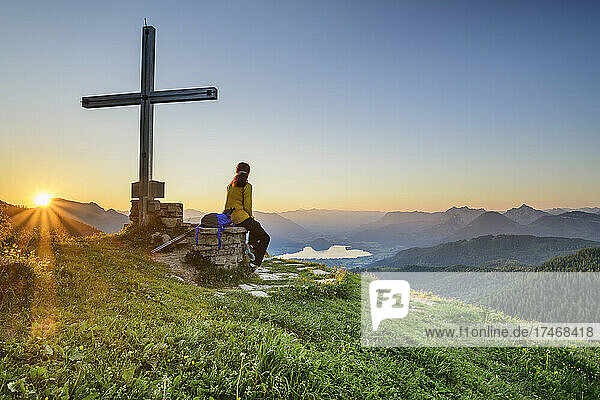 Wanderin sitzt bei Sonnenaufgang am Gipfelkreuz auf dem Berggipfel  Kärnten  Österreich