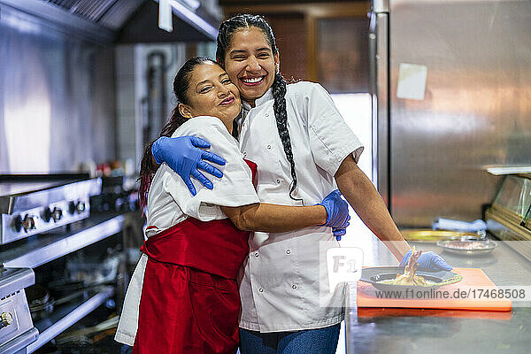 Happy kitchen trainees embracing each other in restaurant