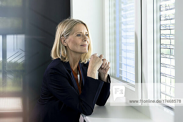 Blond businesswoman contemplating while leaning on window sill