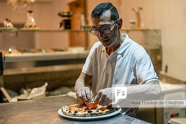 Chef adding toppings on pizza in kitchen