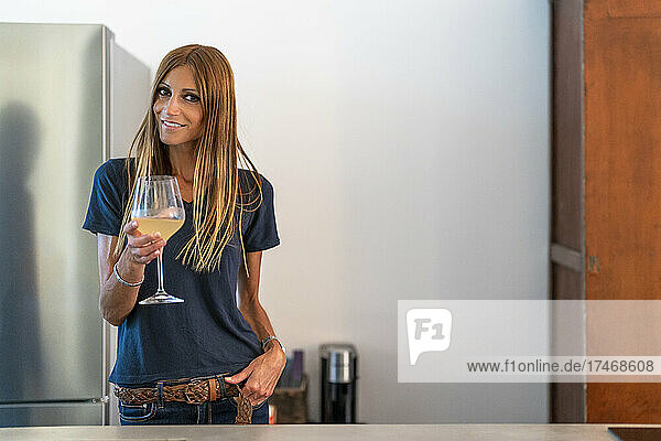 Smiling woman with brown hair holding wineglass in kitchen