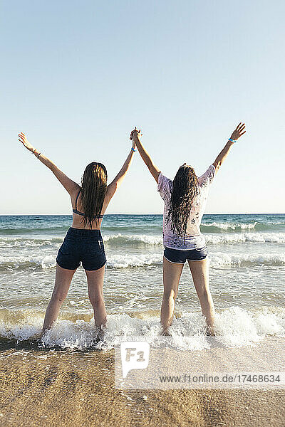 Junge Frauen mit erhobenen Armen genießen am Strand