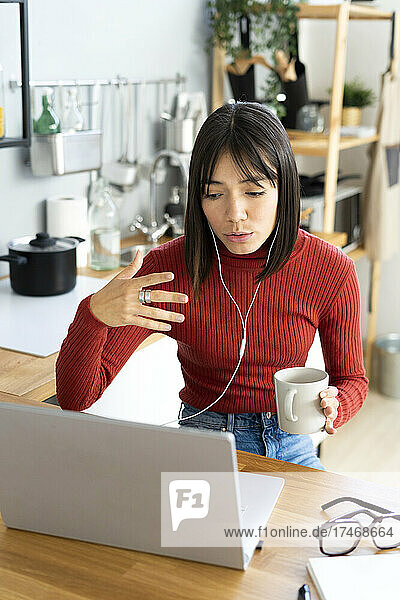 Female influencer gesturing on video call holding coffee mug