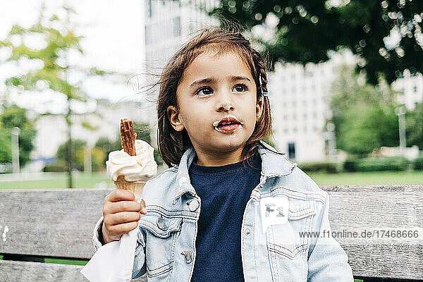 Cute girl with brown hair holding ice cream cone at park