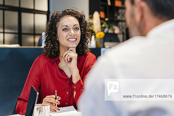 Smiling businesswoman with hand on chin listening to colleague in office