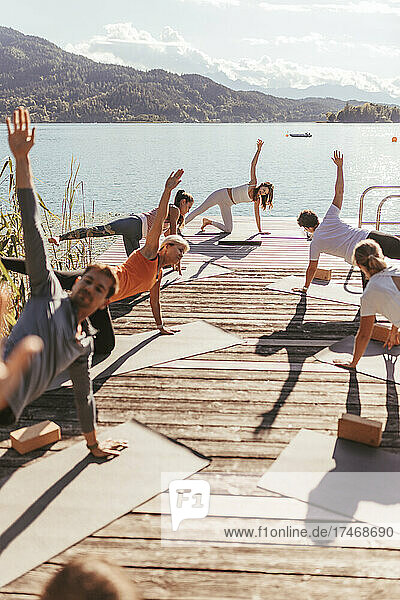 Man and women with hand raised practicing yoga on jetty