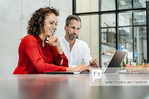 Smiling businesswoman using laptop while working with coworkers in office
