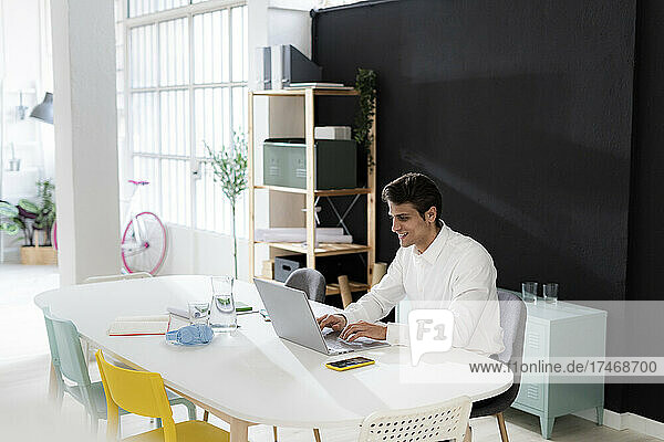 Smiling working man using laptop at desk in office